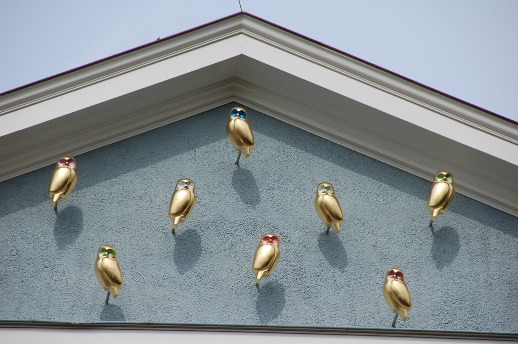 Un fronton al unei clădiri universitare din orașul Groningen, Olanda pe care sunt fixate 8 bufnițe aurii sculptate, cu ochii colorați în diferite culori.