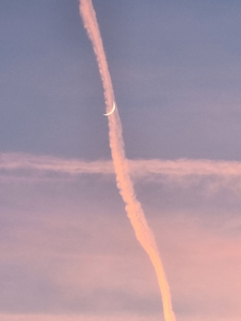 Pe un cer violet, luna în formă de semilună se suprapune peste două urme de siaj de la avioane.