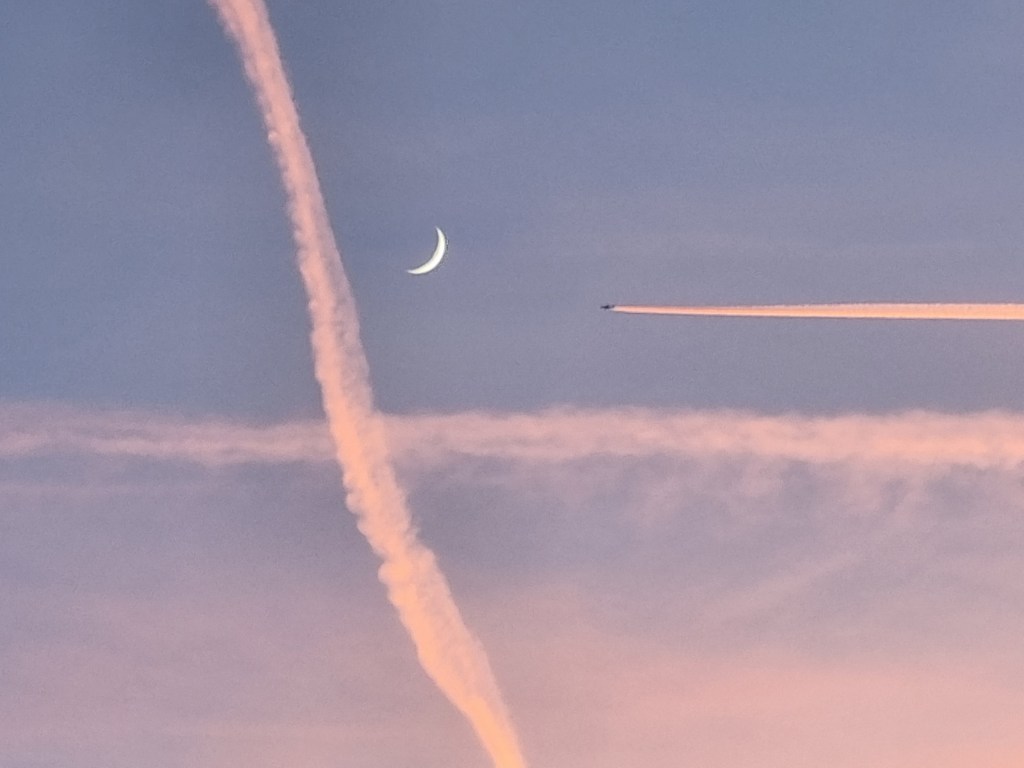 Pe un cer violet, către luna în formă de semilună albă se îndreaptă orizontal un avion. În stânga lunii străbate vertical, ușor înclinată, o urmă de siaj de la un alt avion.