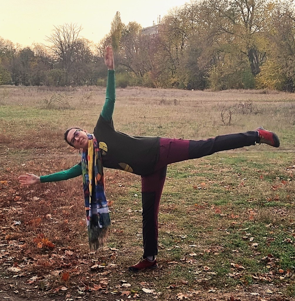 Oana stă în echilibru în poziție de cumpănă laterală, îmbrăcată sport, dar cu un fular lung, multicolor, care atârnă pînă jos. Fundal de toamnă, pe spașiul verde al Turnului de Parașutism.